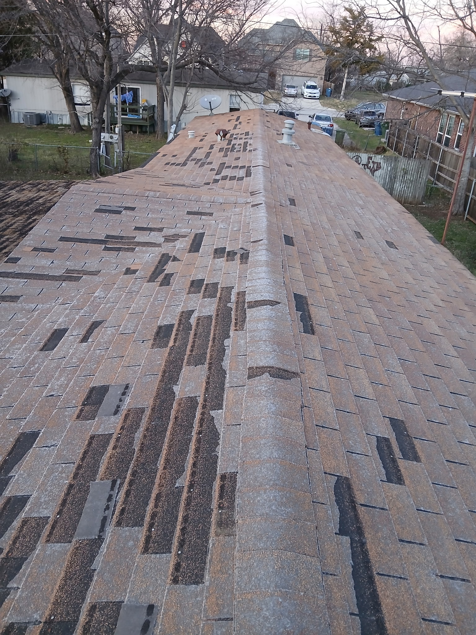 Damaged residential roof with missing and deteriorated shingles before replacement